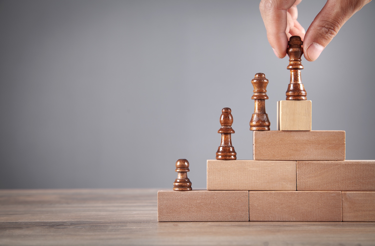 Male hand holding chess piece on wooden blocks.